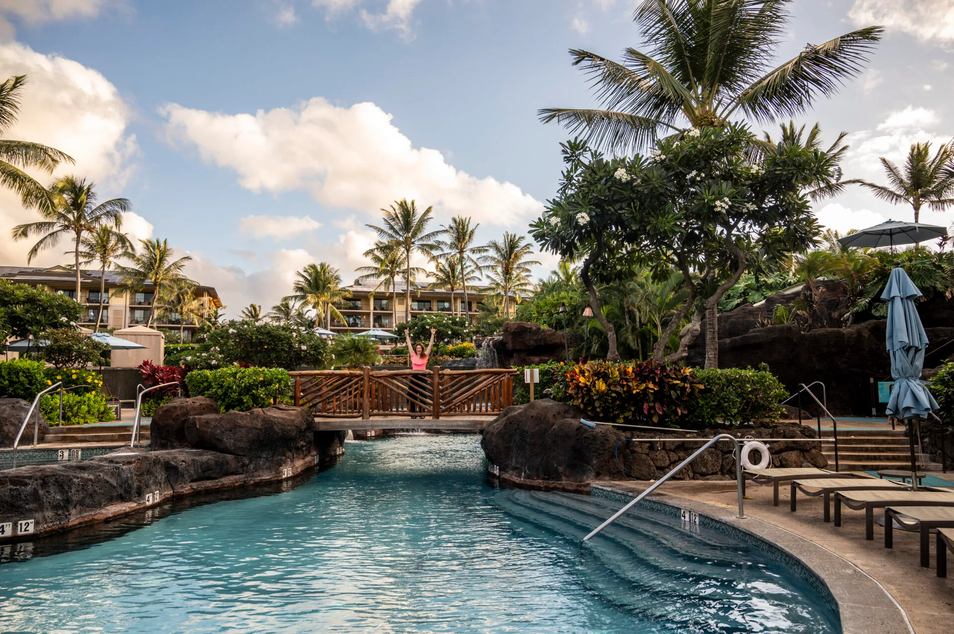 woman stands on walkway bridge over the pool at the best family hotel in Kauai, Koloa Landing Resort