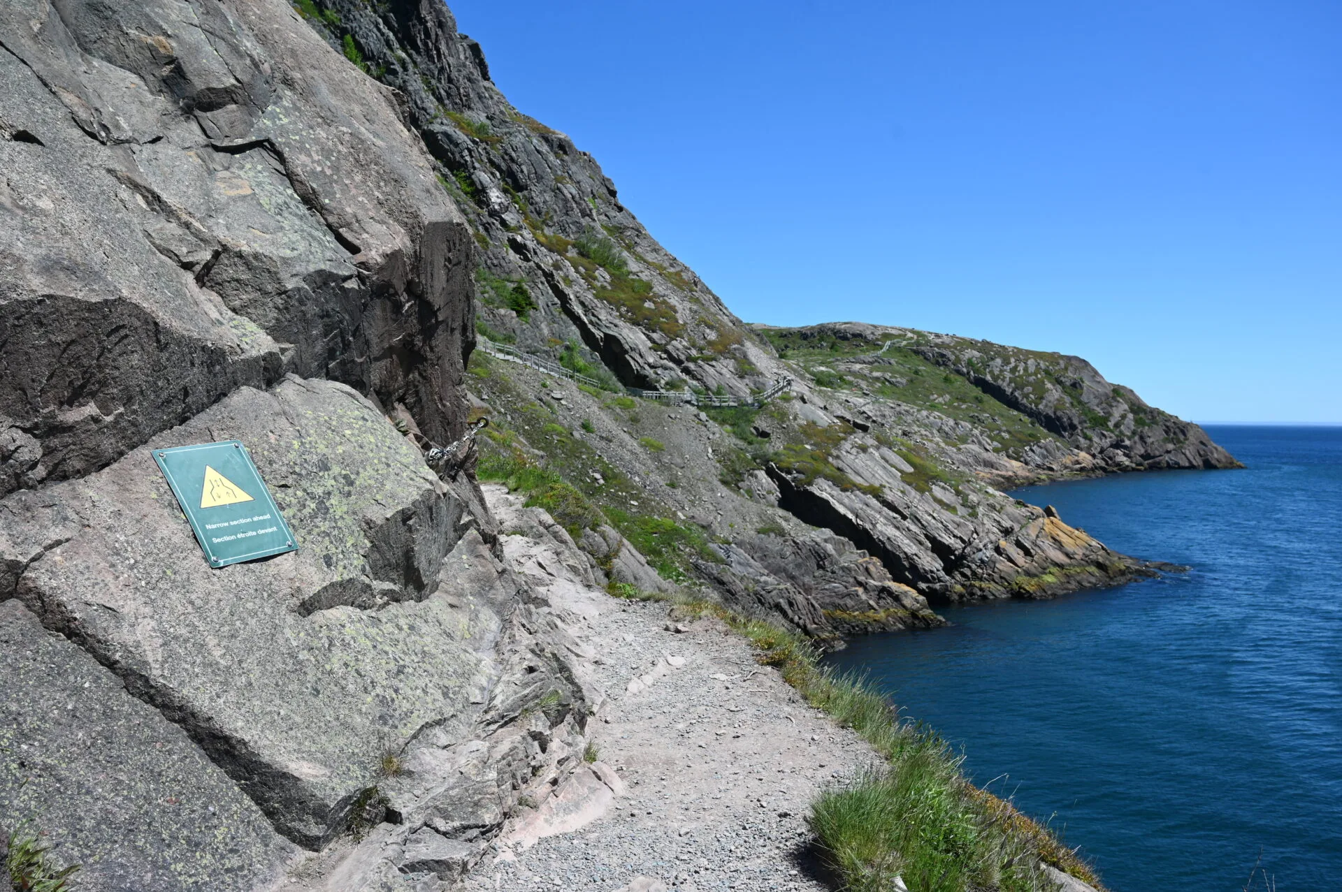 rocky cliffs alongside the ocean with the north head trail head sign and trail in the background