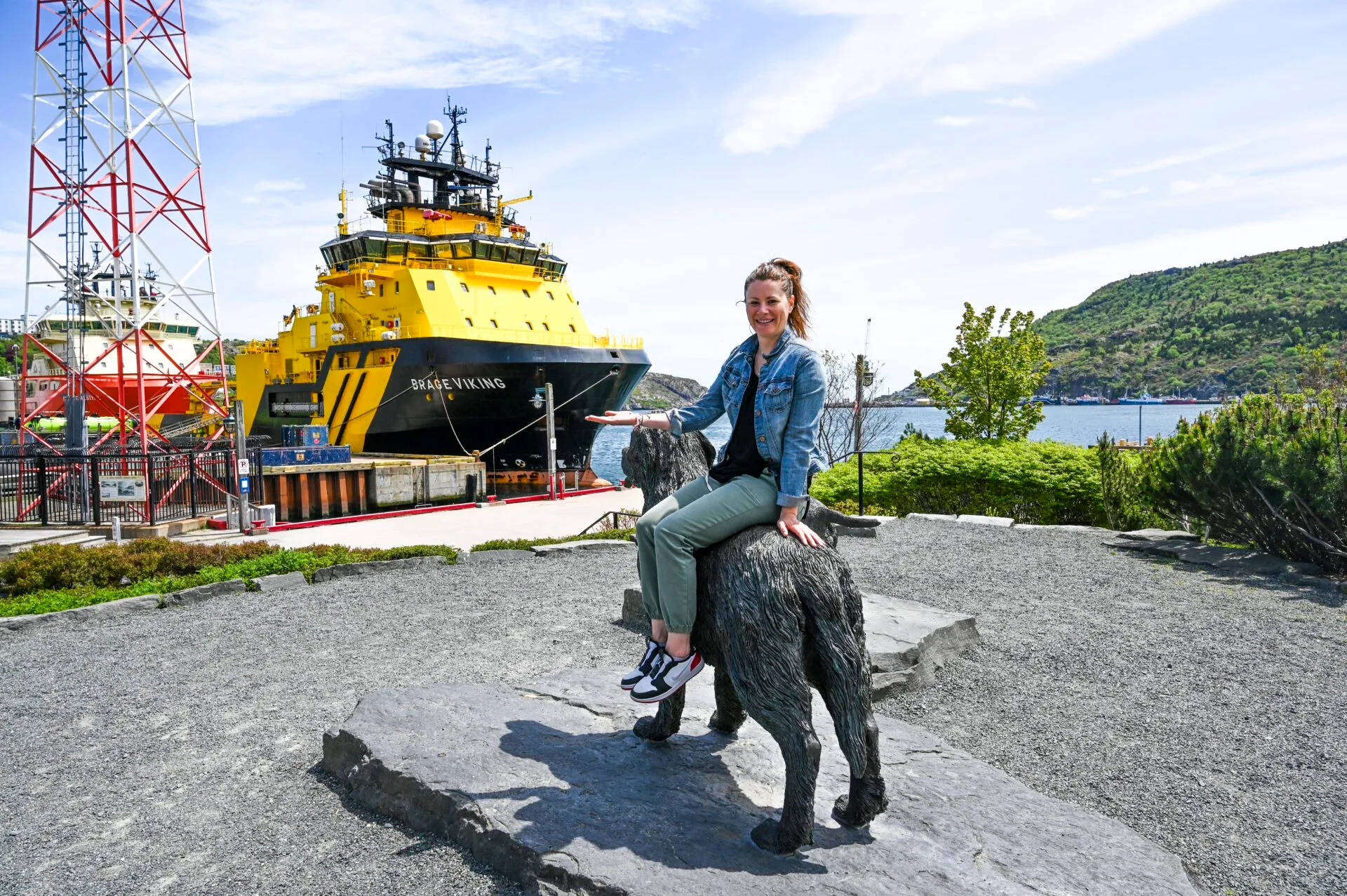 a woman sits on a newfoundland dog statue in harbourside park in st. john's