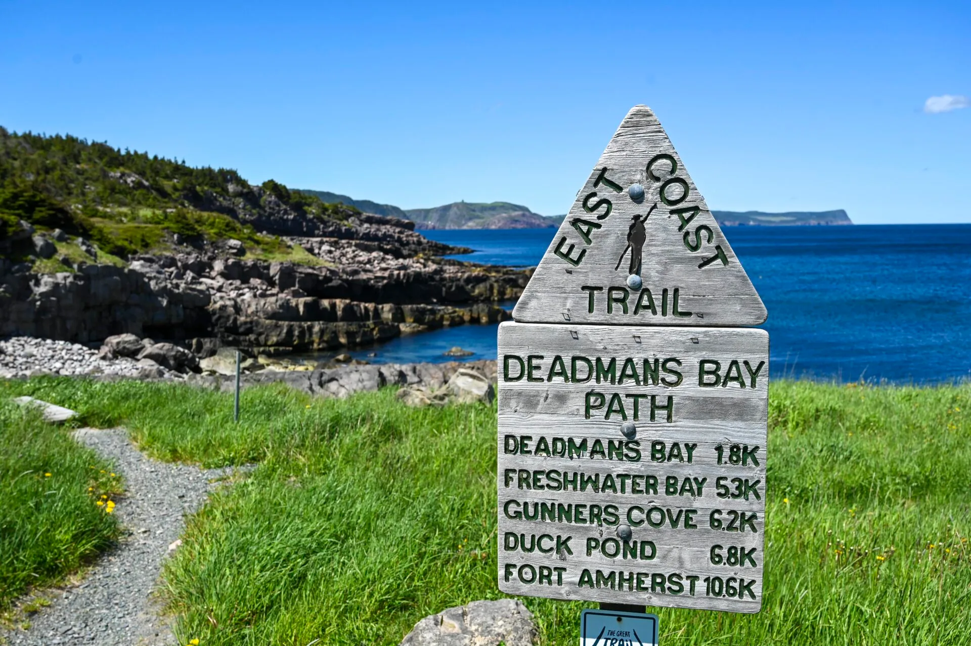 deadmans bay path sign at the trailhead of the east coast trail, a rocky coastline and ocean is behind the sign