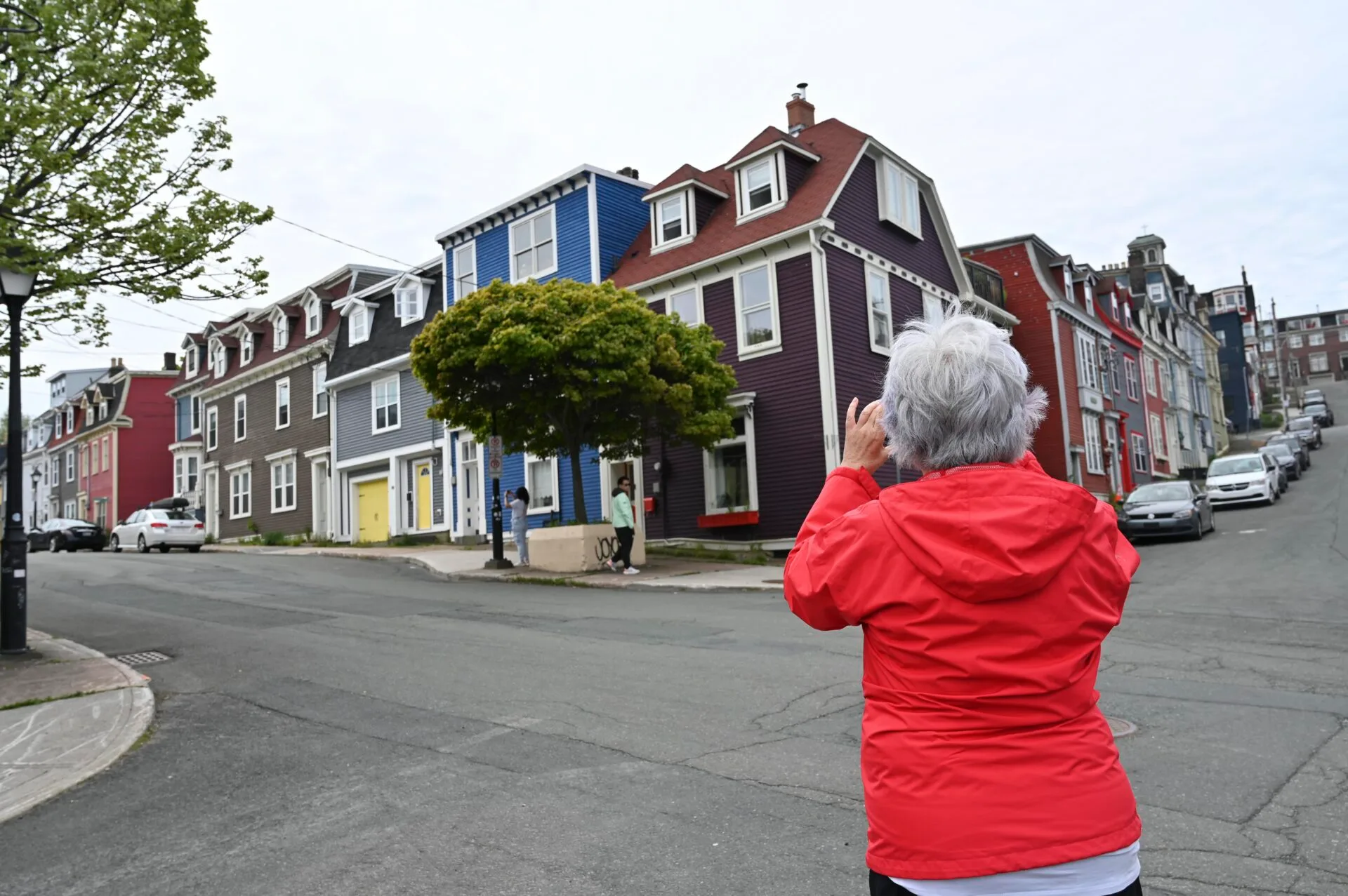 a woman with her back to the camera is taking photos of historical houses in downtown st. john's