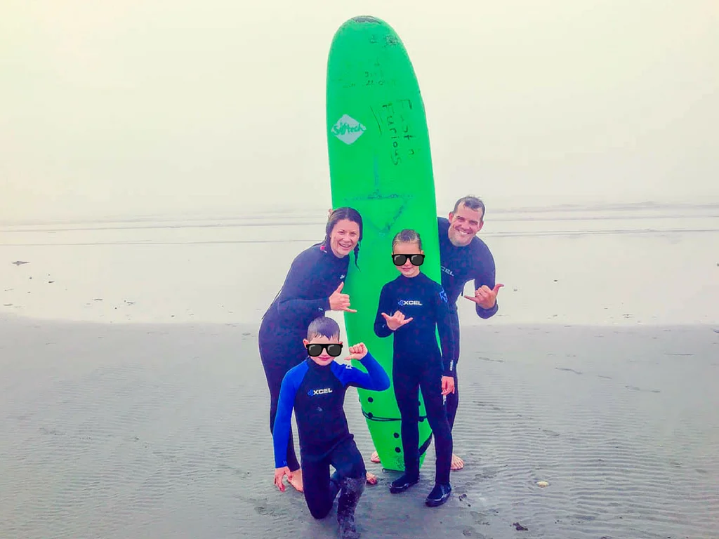 Family posing with surf board on beach for bc road trips activity