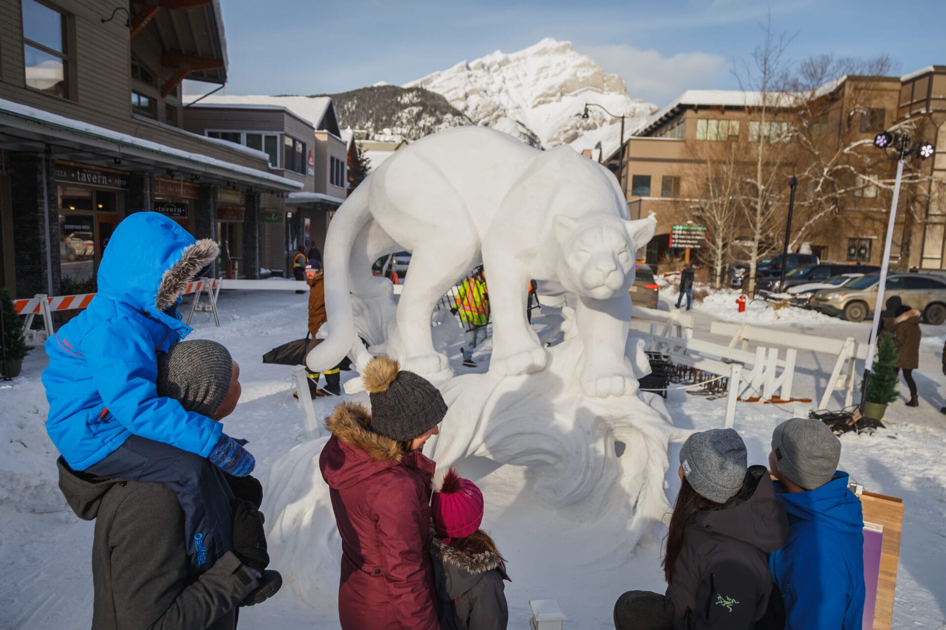 a family looks at a snow sculpture of a large mountain lion at banff snow days festival