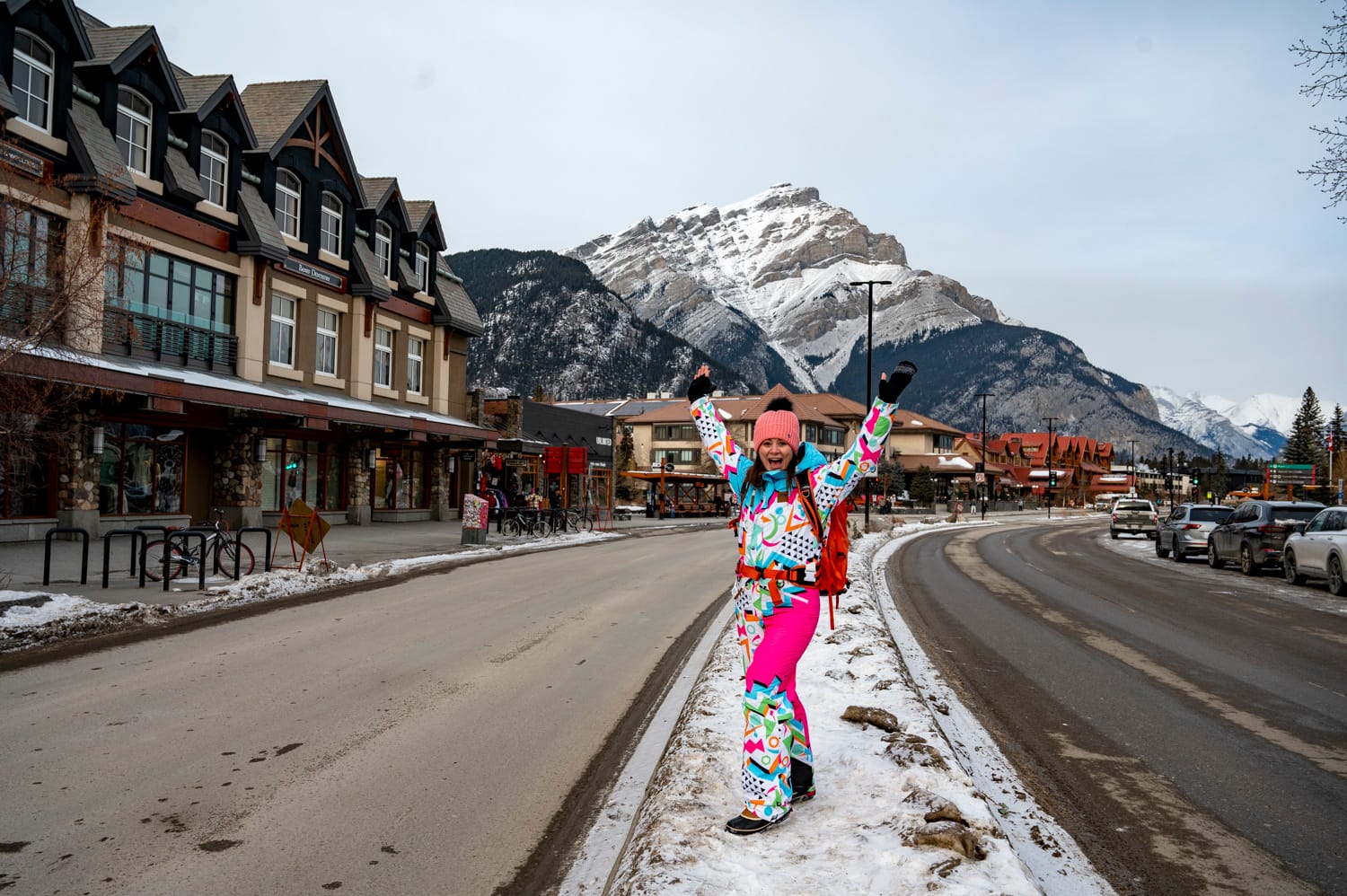 a woman stands in the middle of downtown banff wearing a bright coloured snow suit during the banff snow days festival