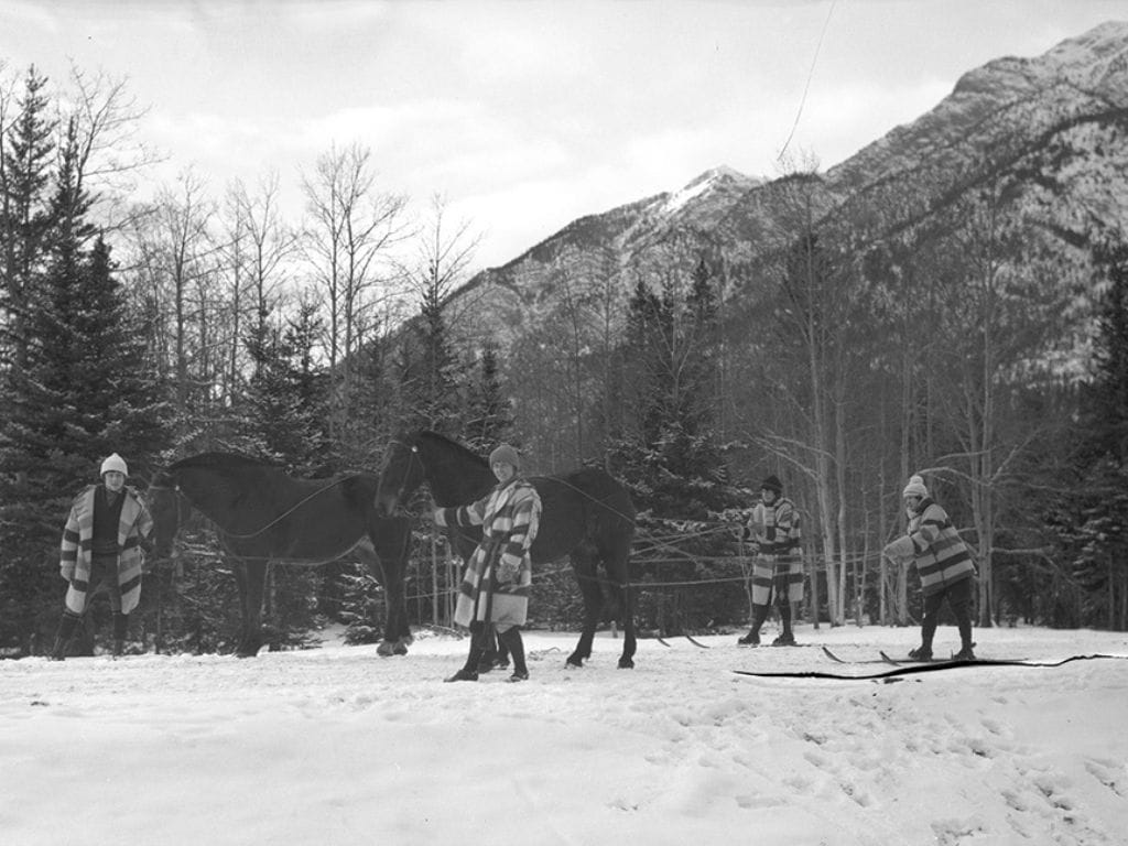 historic black and white photo of four people and two horses taking part in skijoring during 1924
