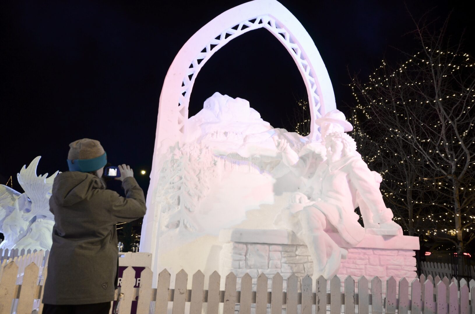 Girl taking a photo of a snow sculpture of scenery at Banff SnowDays Festival