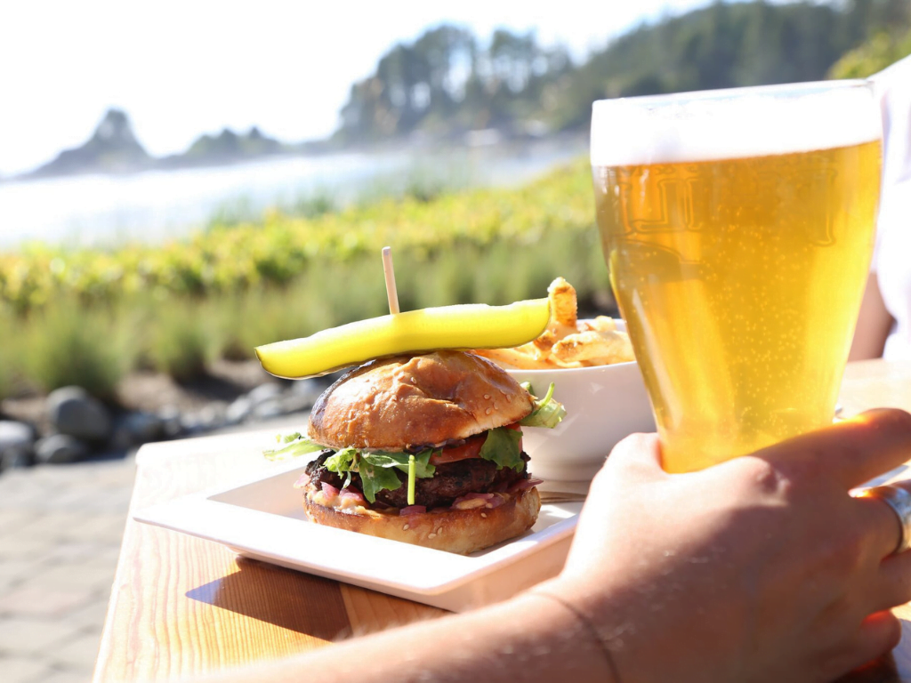 a mouthwatering burger and cold beer sitting on a table that overlooks the view from the sandbar bistro