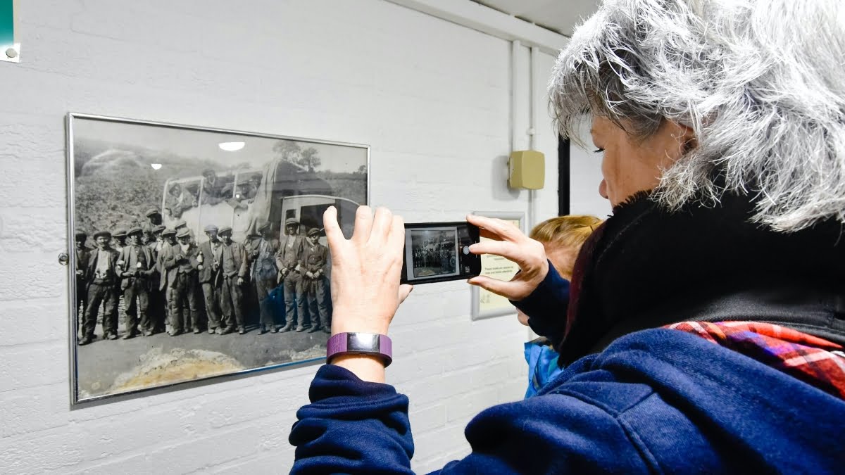 Woman taking photo on her phone of a photo of men who worked at a coal mine inside a museum