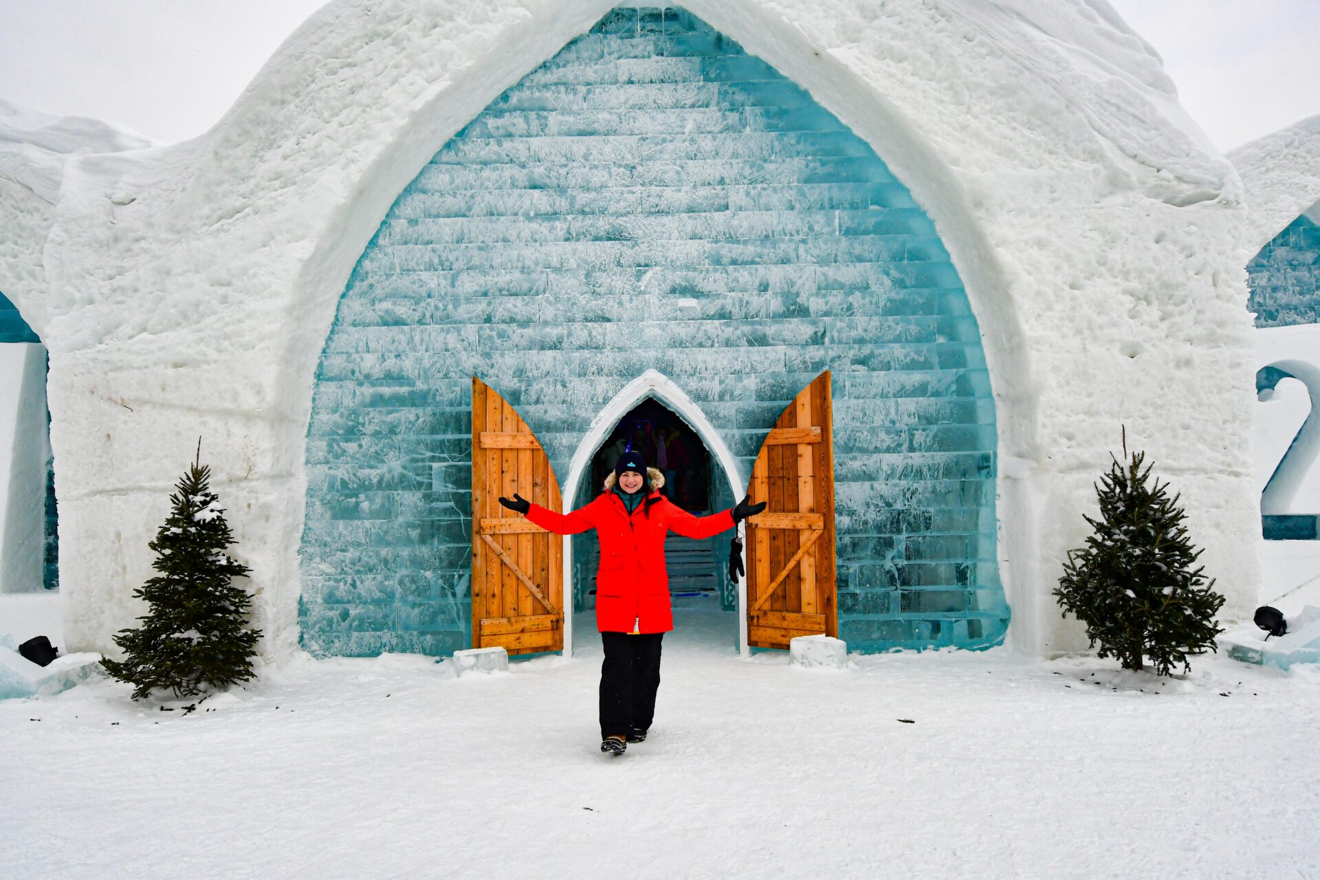 woman wearing a red coat stands outside the entrance of the Hôtel de Glace