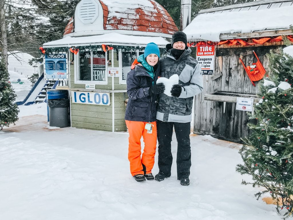 couple stand in front of ticketing building holding a heart shaped snowball at snow tubing montreal