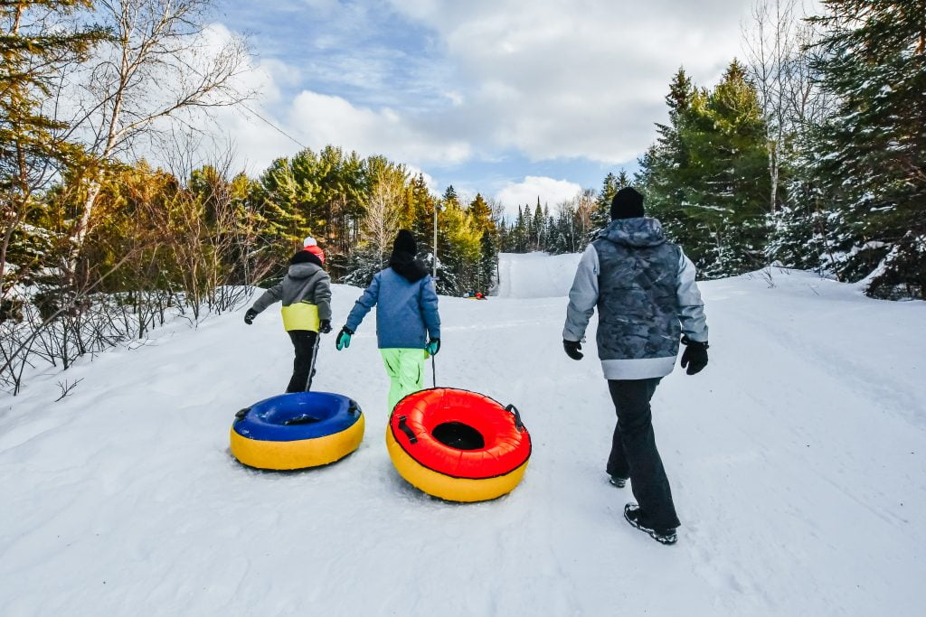 Man and two children walking up a hill with snow tubes at chalets lanaudiere