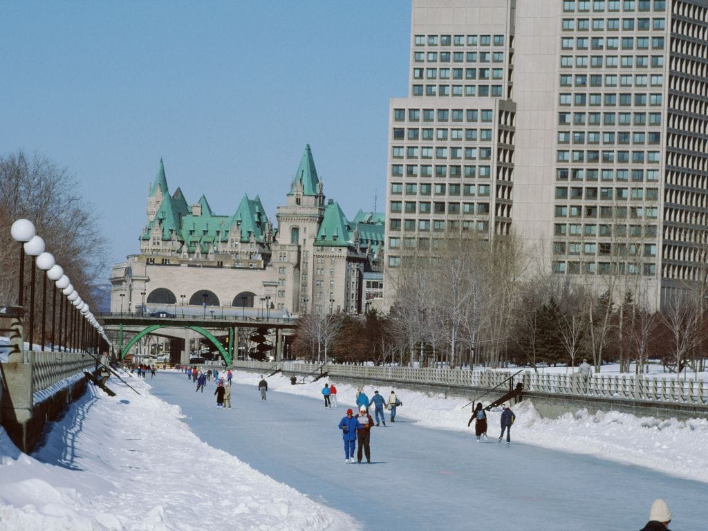 lots of people skating on the rideau canal, downtown buildings are behind them