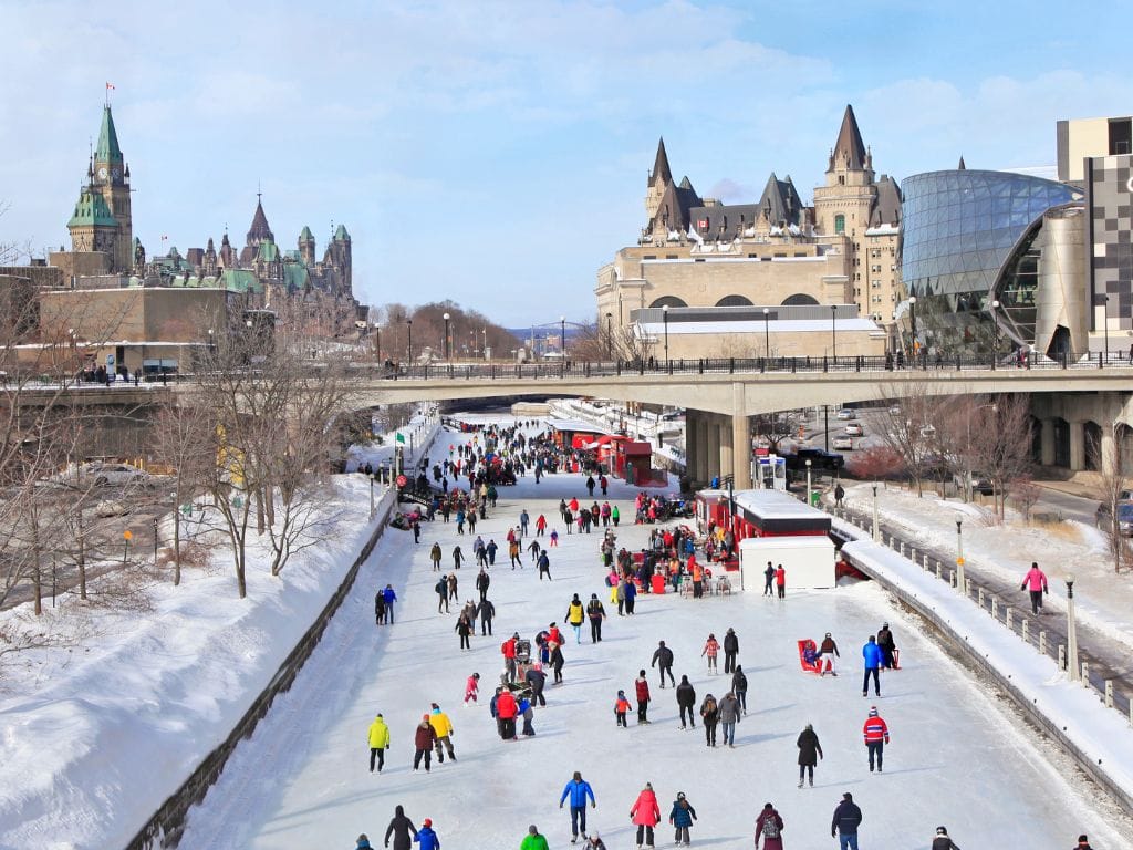 a colourful rainbow of people skating on the rideau canal, downtown is in the background