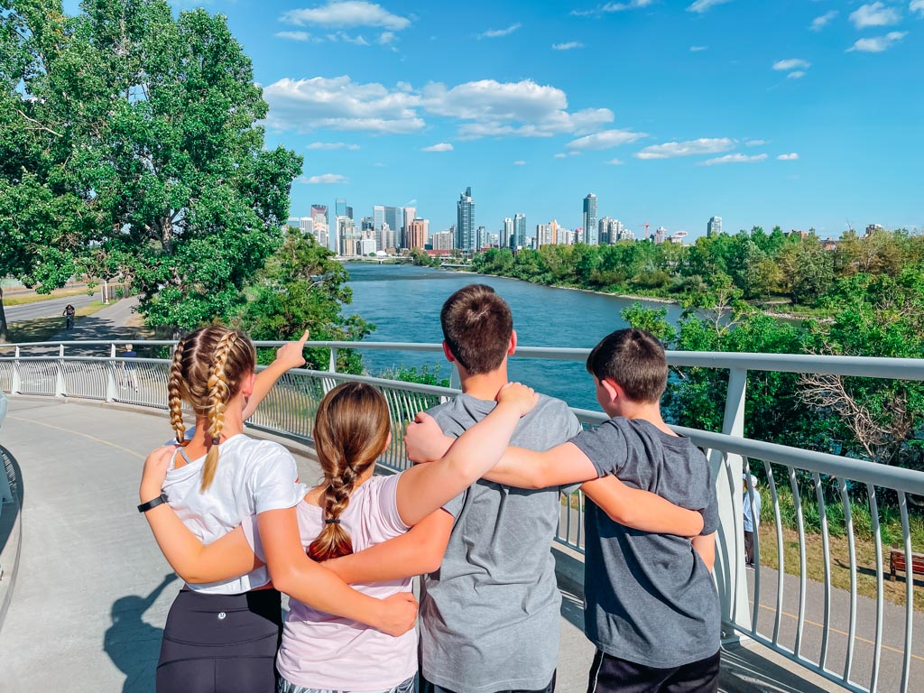 four kids with linked arms overlooking the bow river in calgary