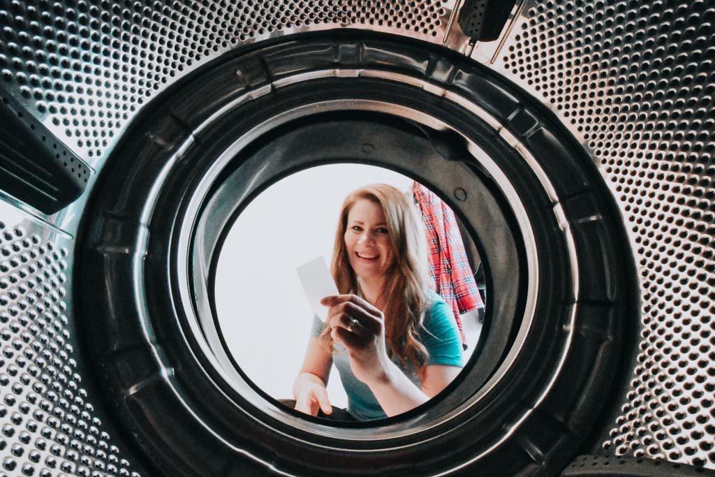 photo taken from inside a washing machine as a woman sits outside holding tru earth laundry strips