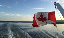 canada flag blowing in the wind on the back of a ferry on the ocean