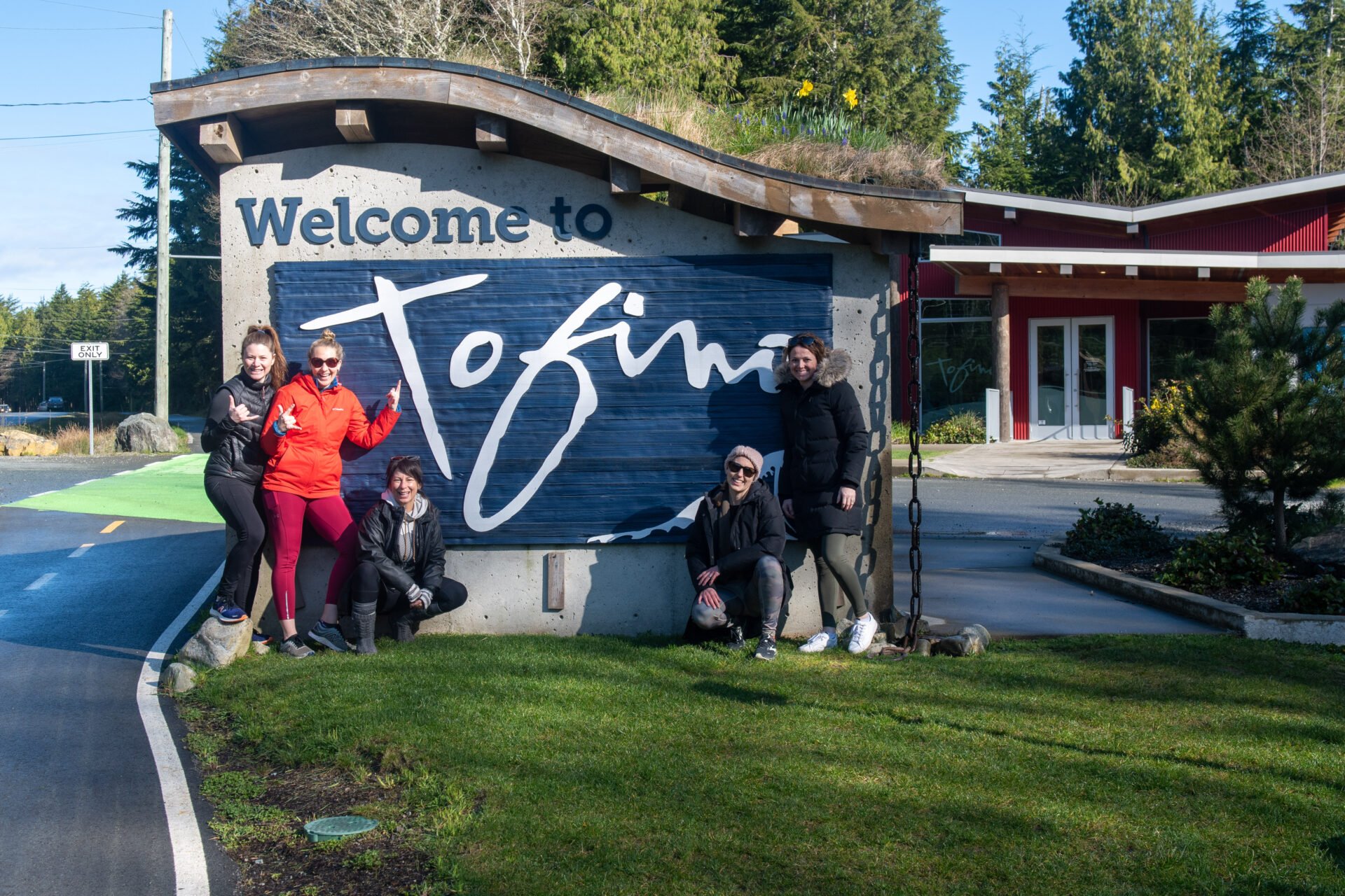women standing in front of the welcome to Tofino sign on their Tofino Girls Getaway