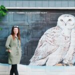 woman standing next to a large snowy owl mural painting on a garage door