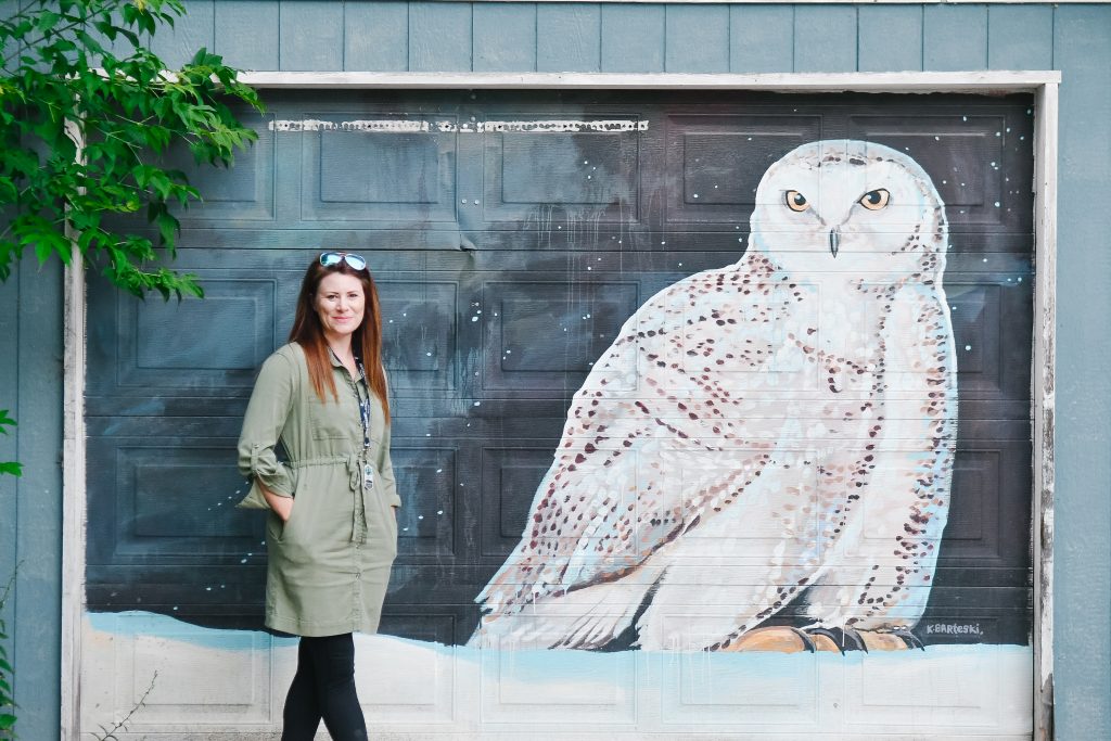 woman standing next to a large snowy owl mural painting on a garage door