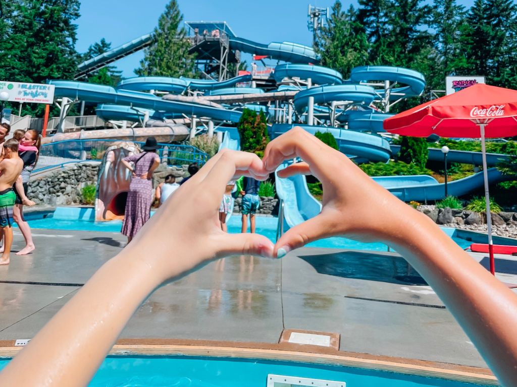 two friends making a heart with their hands in front of the waterslides at cultus lake waterpark