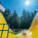 people on a tube splashing in the bottom pool of a large yellow valley of fear waterslide