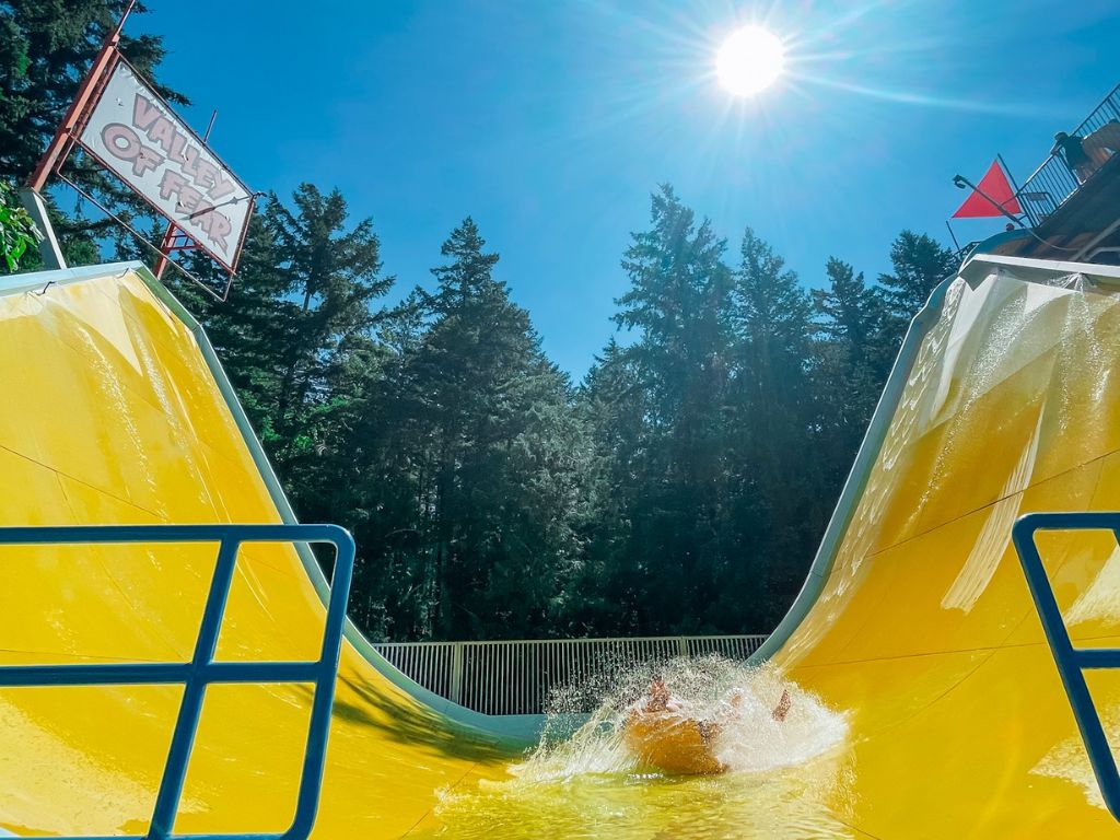 people on a tube splashing in the bottom pool of a large yellow valley of fear waterslide