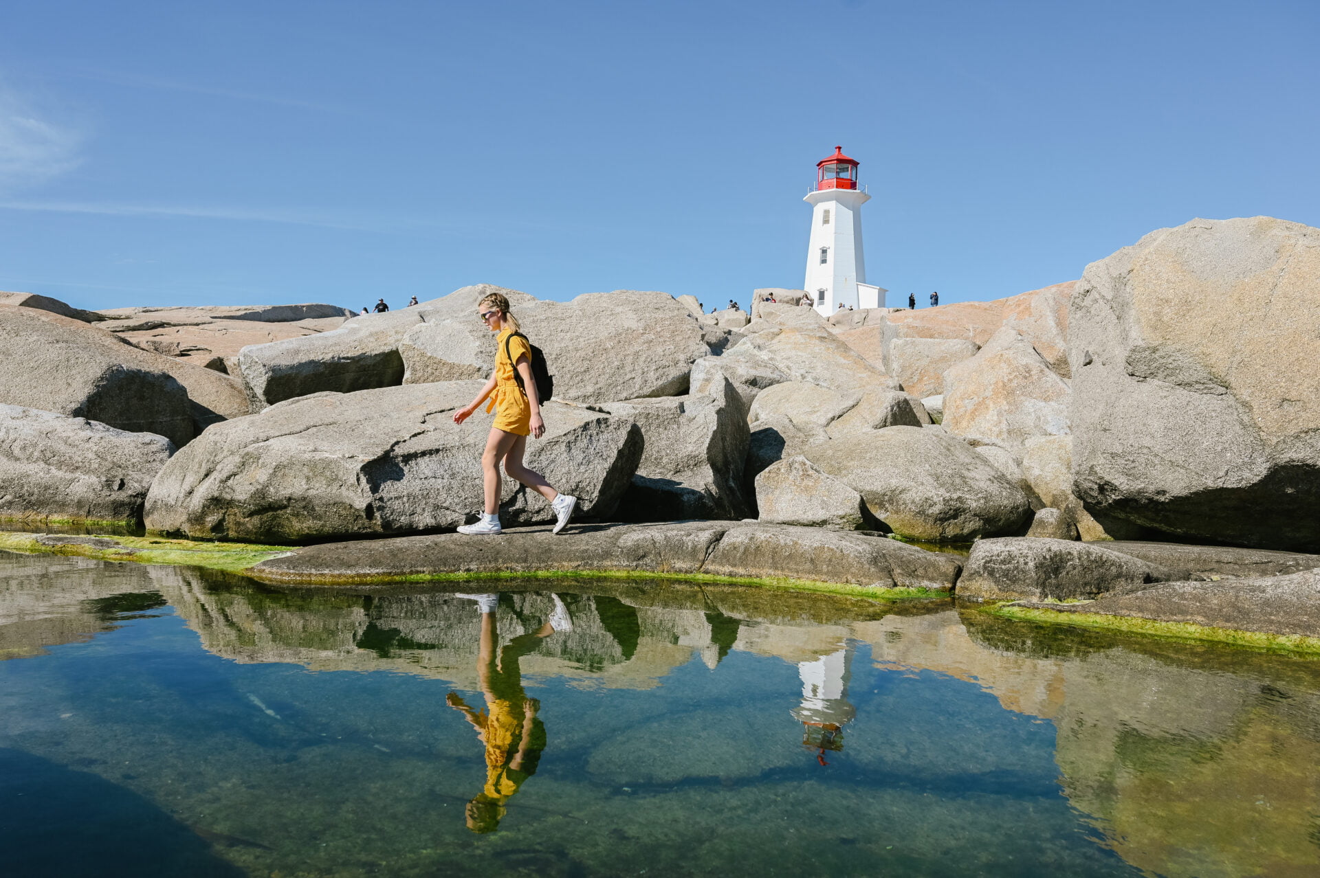 girl walking along waterfront with the peggys cove lighthouse behind her on our Nova Scotia RV road trip