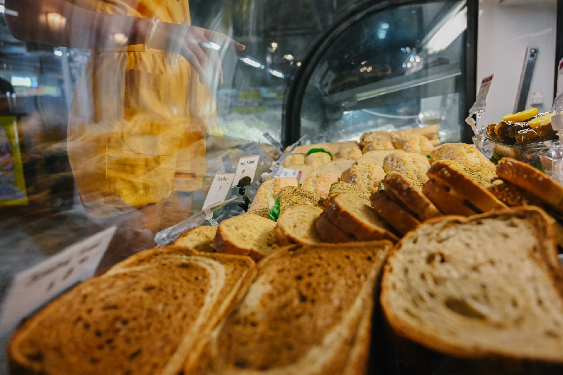 close up of fresh sandwiches while a person points through the glass at their selection