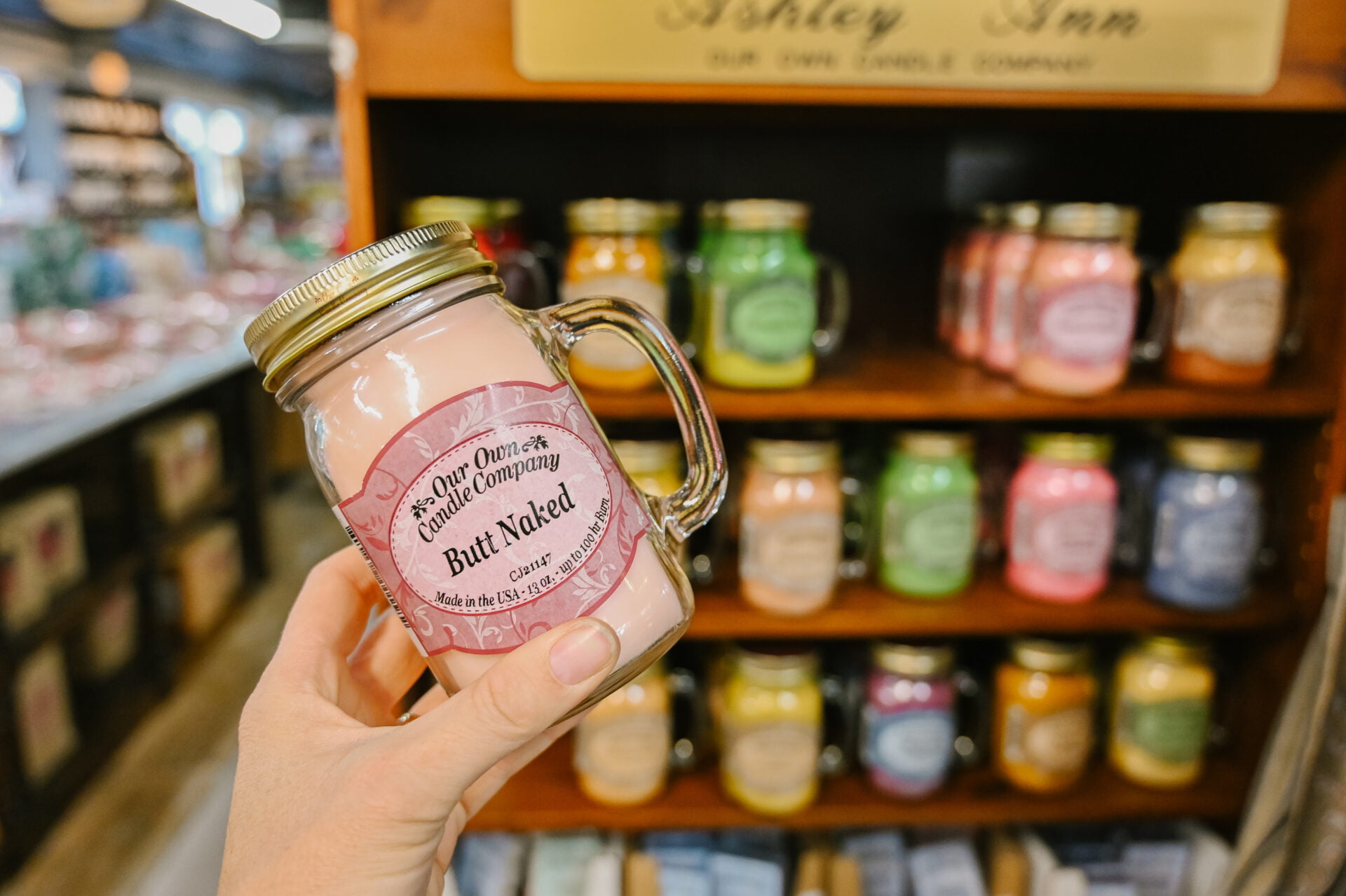 person holding a pink candle in a jar that reads butt naked