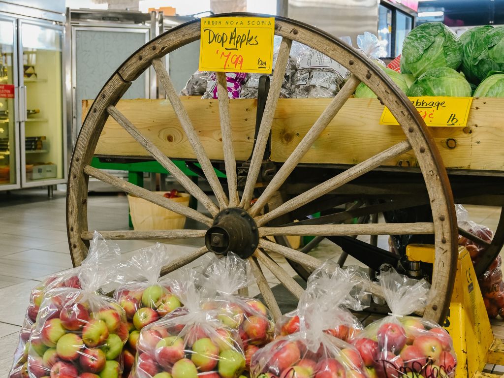 apples in large bags sitting next to an old wagon wheel at the bedford basin farmers market