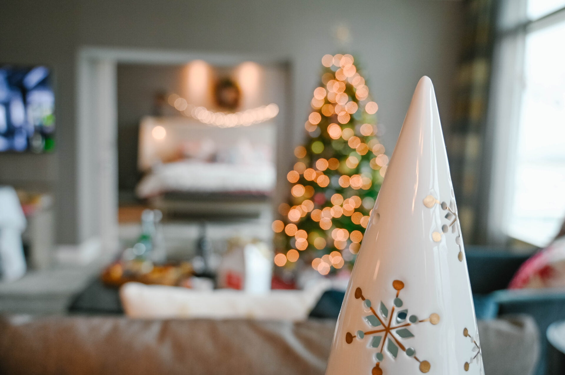 close up of white ceramic christmas tree with a lit up green tree in the background