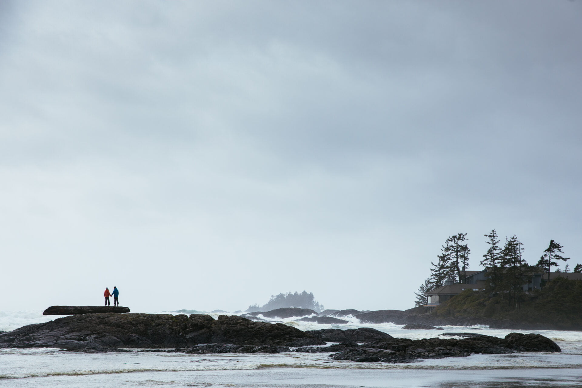 a couple holds hands while standing on a rock in the ocean off the coast of tofino