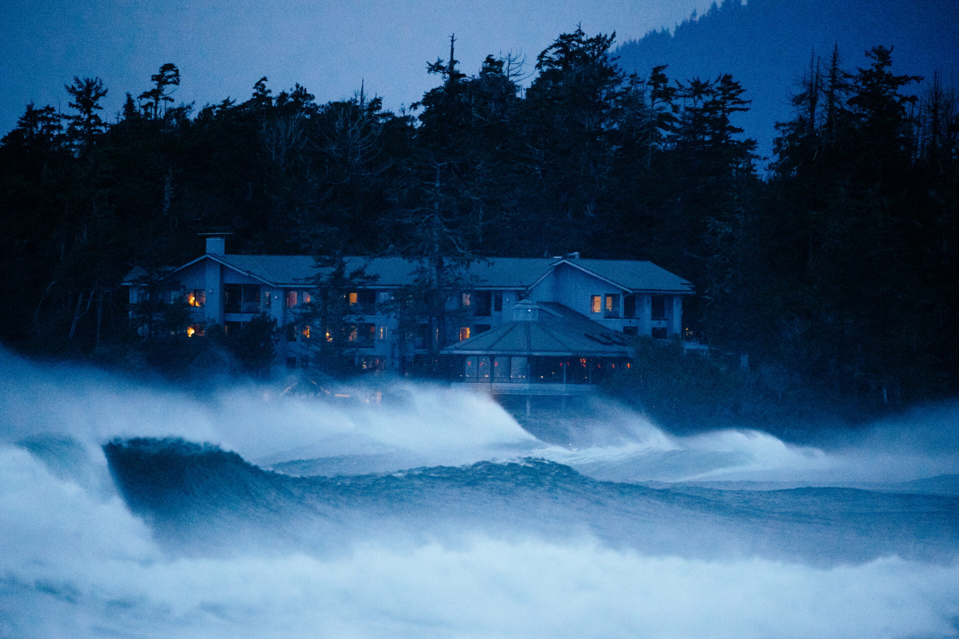 close up view of the wickanninish inn, the best storm watching hotel in tofino, surrounded by huge crashing winter storm waves at dusk.