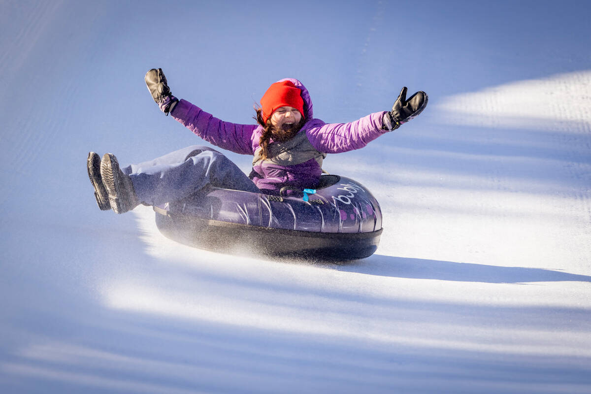 girl with hands up in the air while tubing quickly down the hill at the whistler tube park