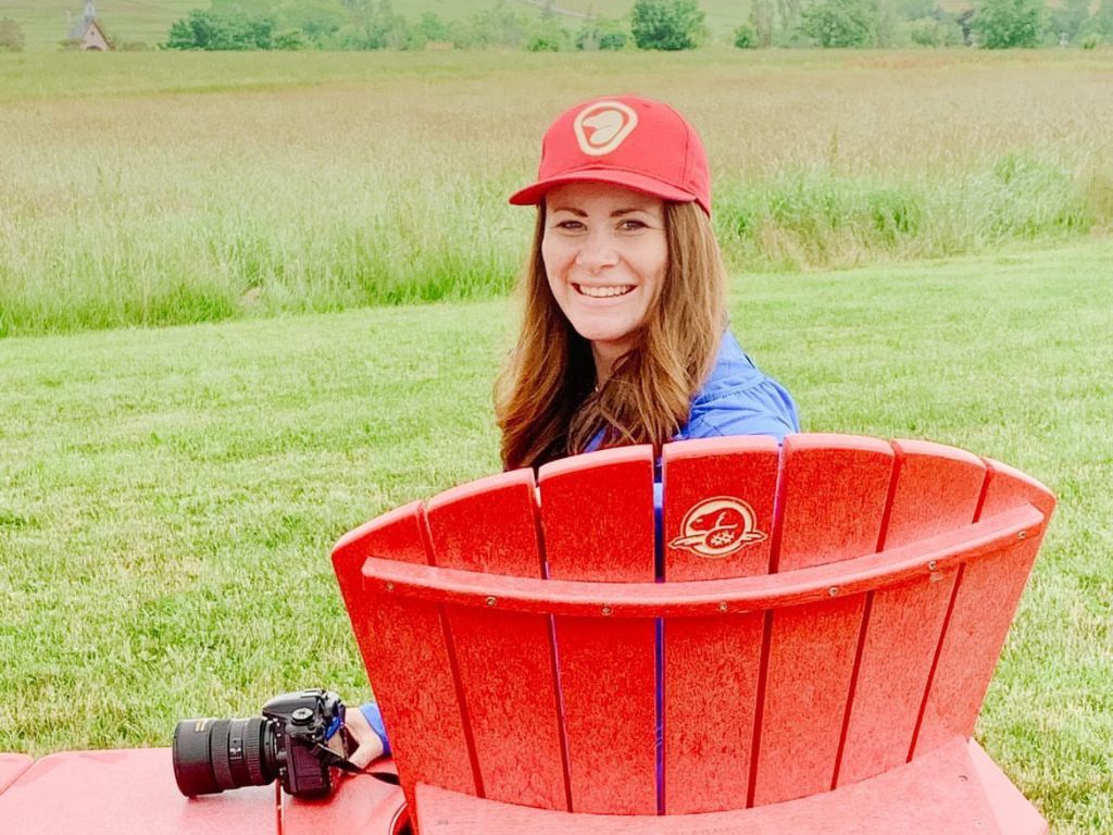 jami sitting on a red parks canada chair, wearing a parks canada hat with her camera beside her wondering is blogging worth it?