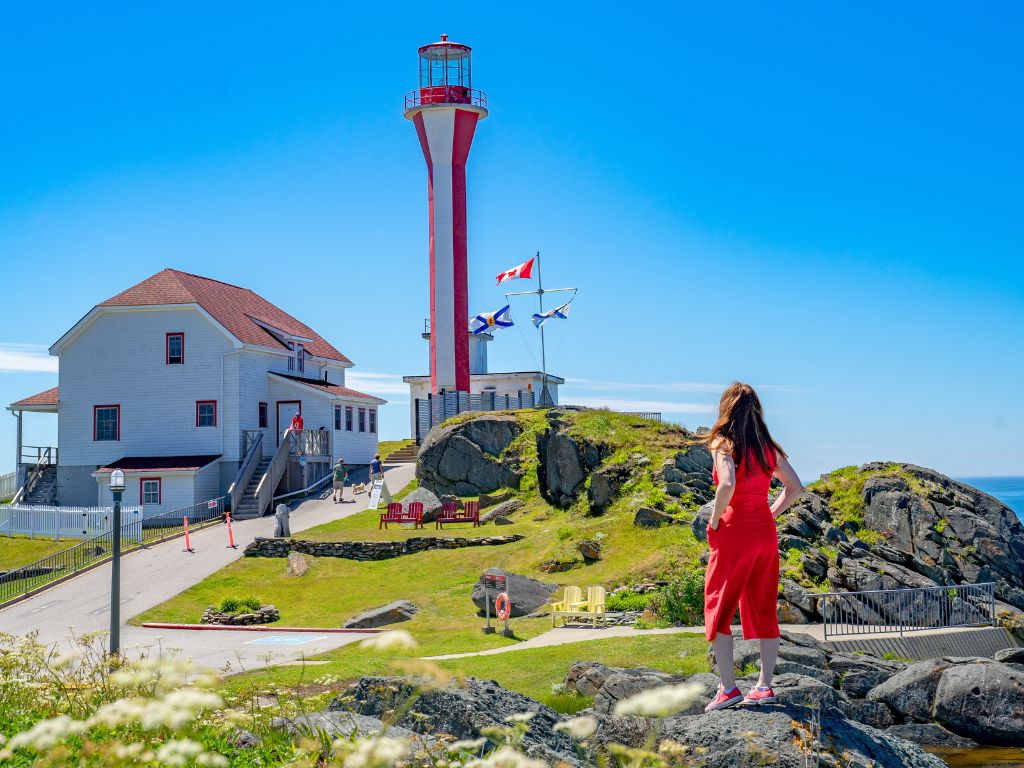 jami stands on the rocks in nova scotia looking at a lighthouse