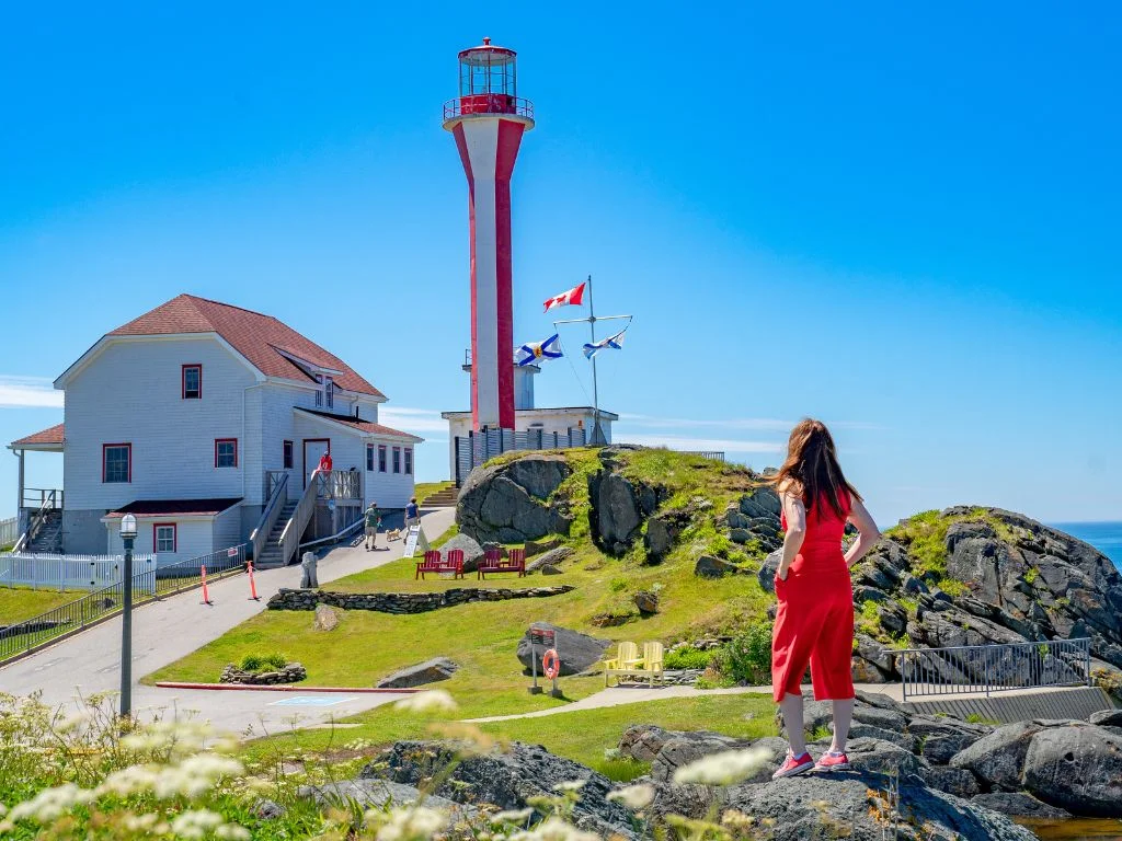 jami stands on the rocks in nova scotia looking at a lighthouse
