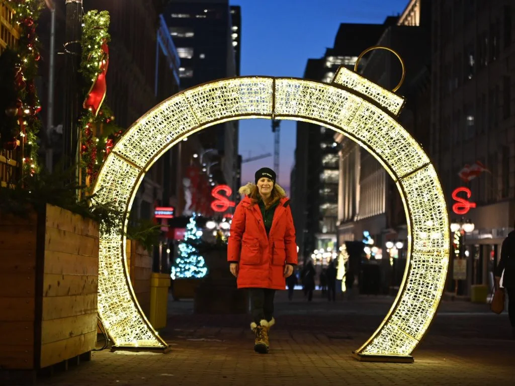 woman in a red parka standing inside a large lit up christmas tree ornament - what to do in Ottawa in November