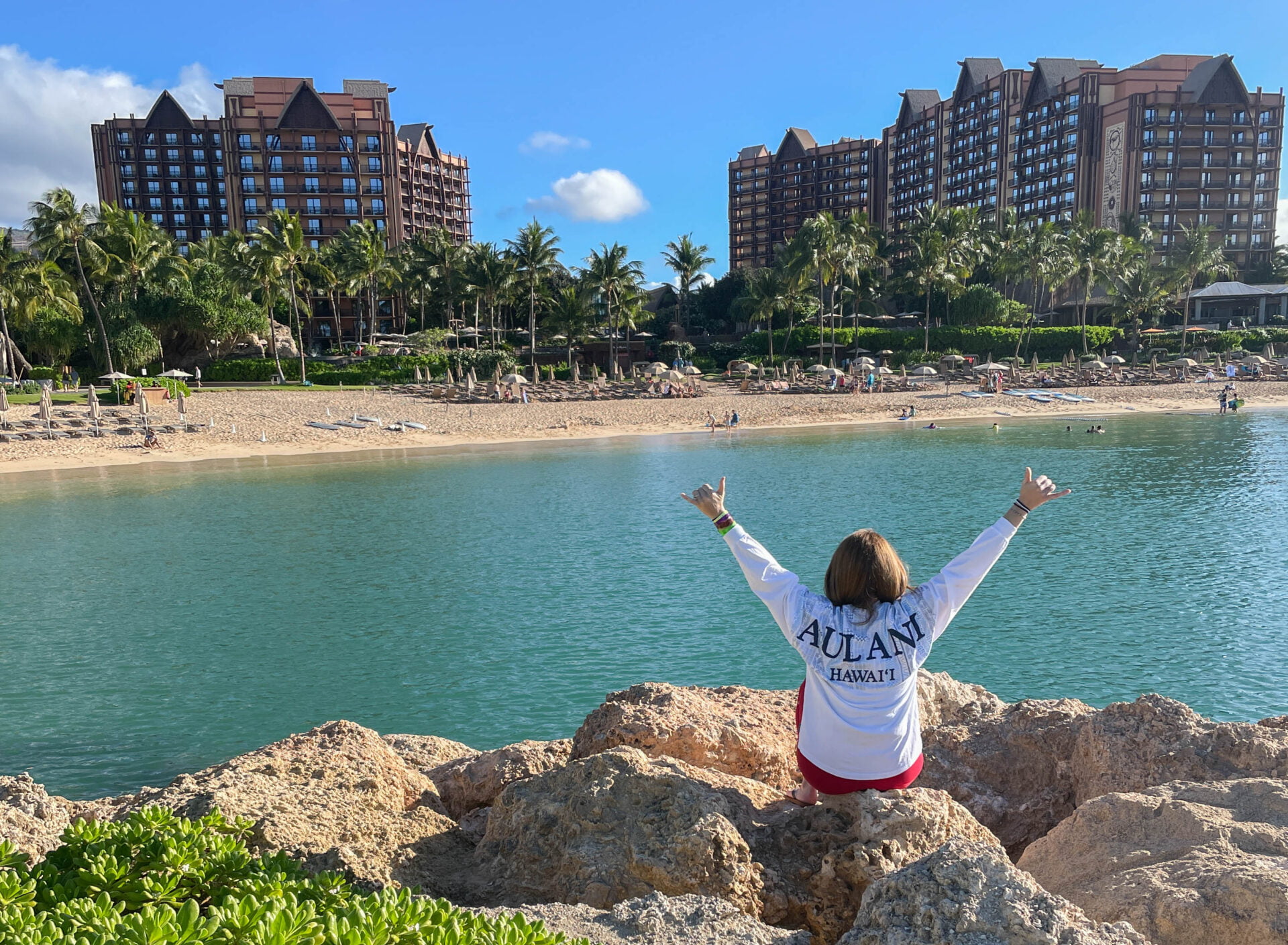 jami with arms in the air sitting across the lagoon from the aulani a disney resort and spa