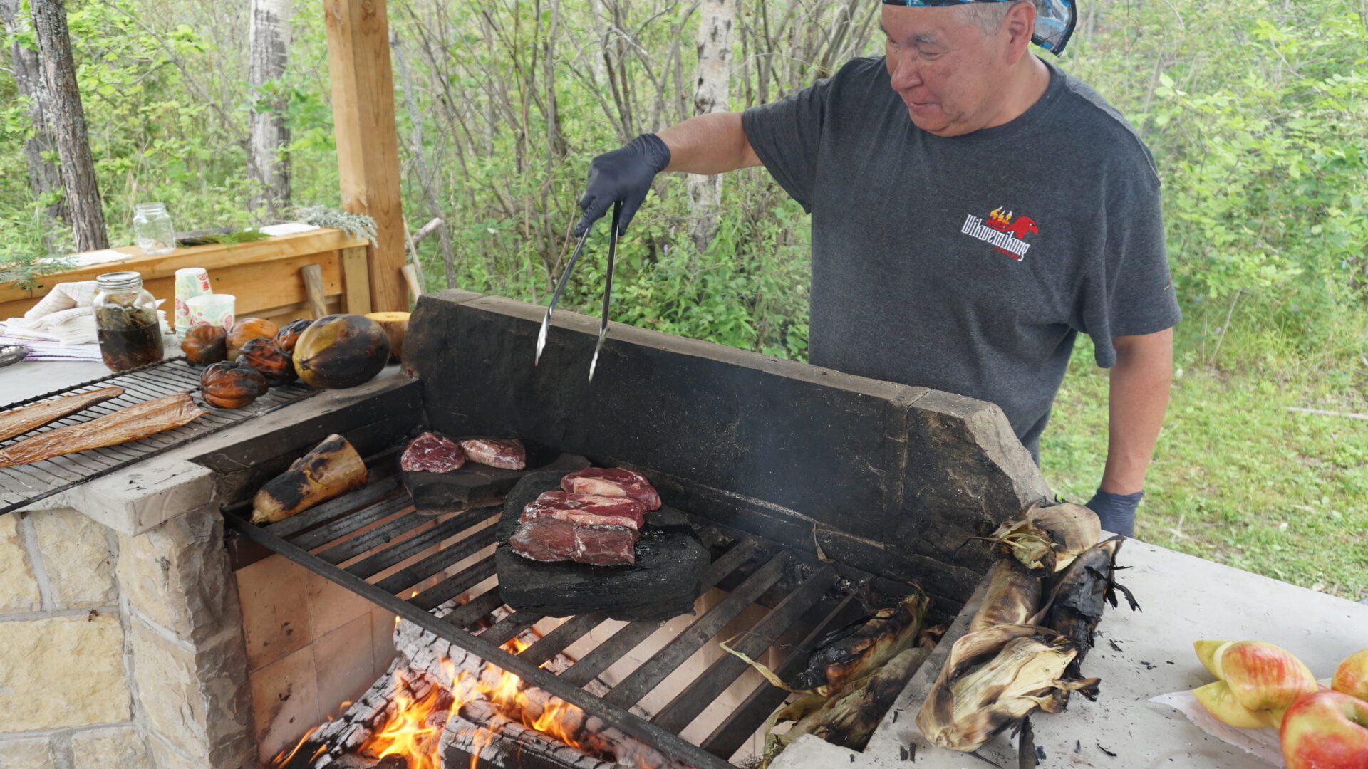 man cooking venison on a rock over a wood buring fire, an Indigenous cultural experience