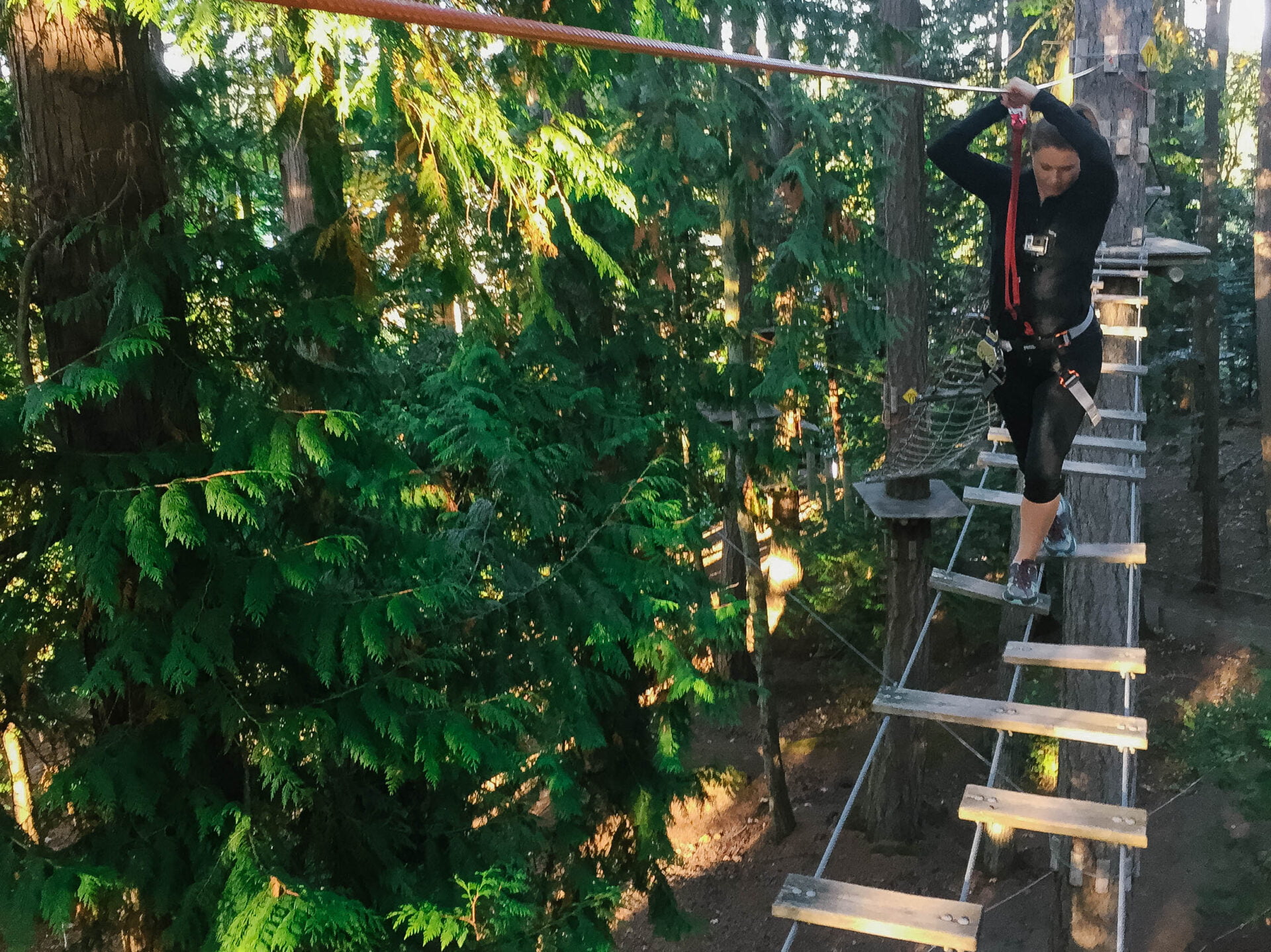 woman navigating a suspended ladder bridge up in the trees of the ropes course