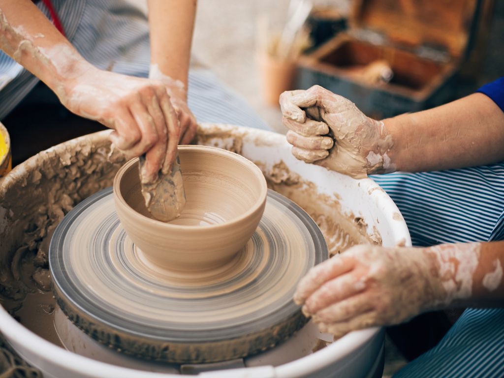 two people making a ceramic bowl on a pottery wheel