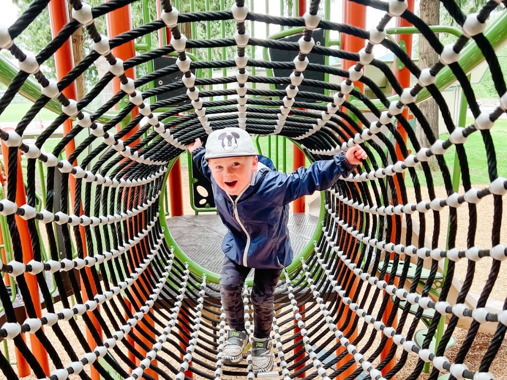 boy wearing a mickey mouse hat climbing through a rope tunnel