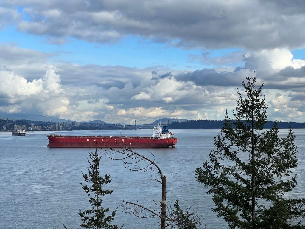 view of a barge floating in the ocean with lions gate bridge and stanley park off in the distance