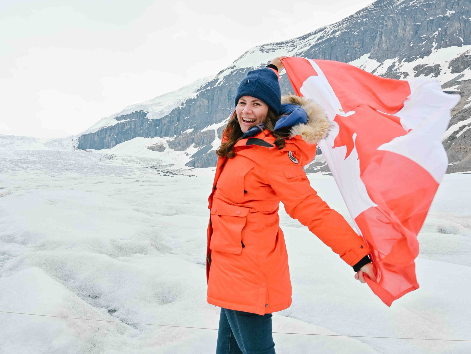 woman standing on athabasca glacier holding a canadian flag behind her blowing in the wind