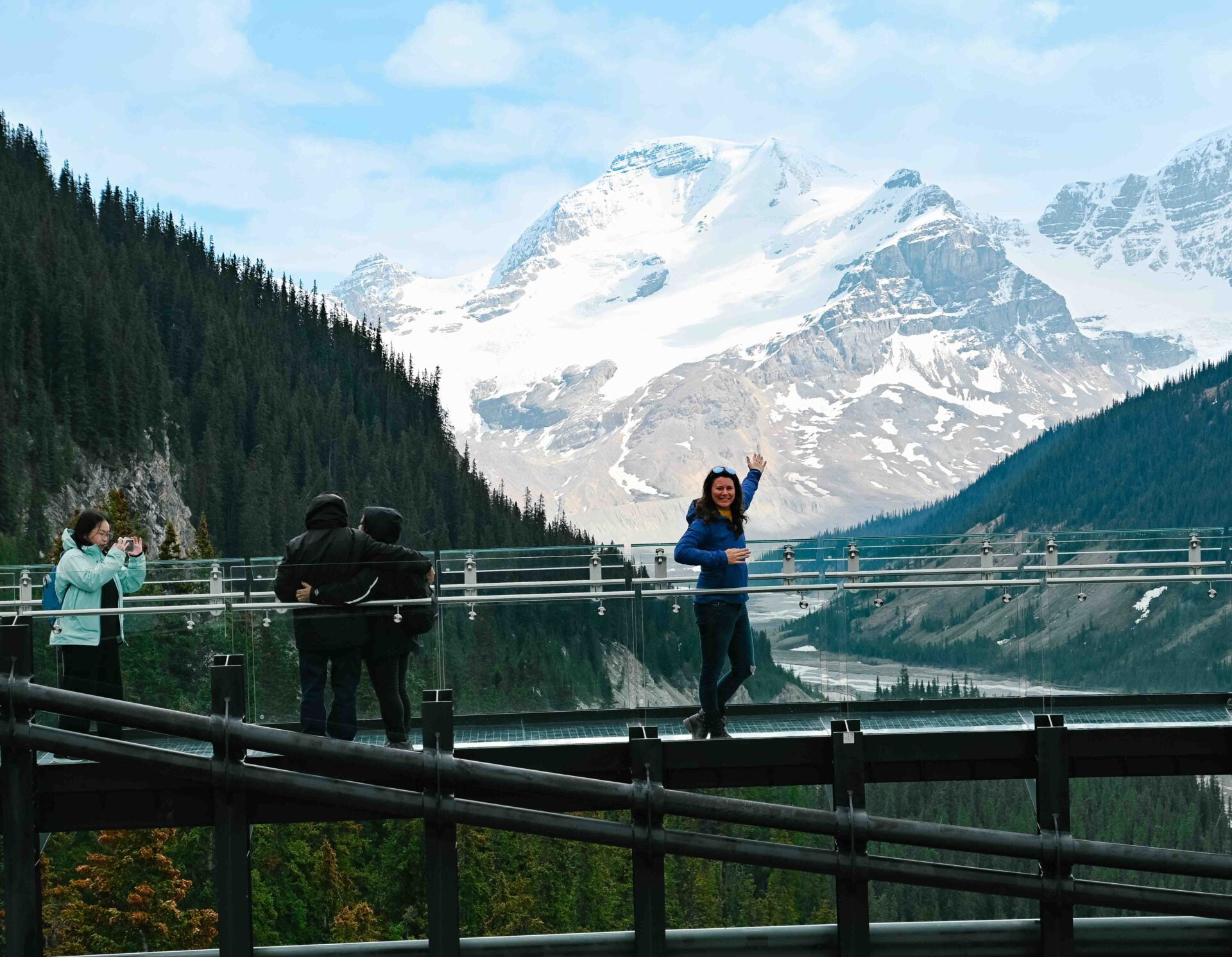 woman with her arm outstretched while standing on the glacier skywalk with the glacier and rocky mountains in the background