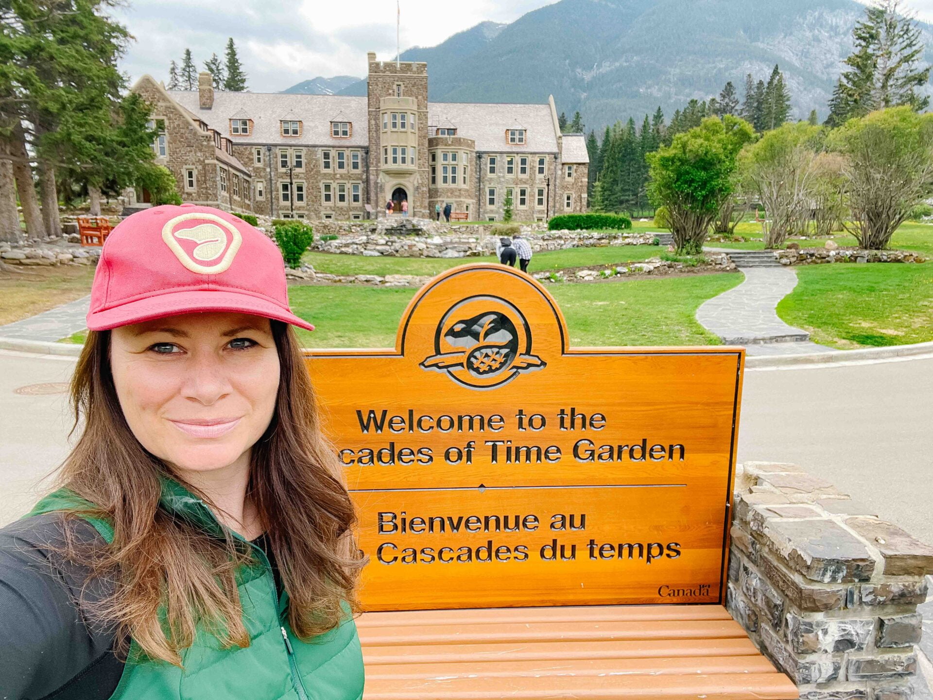 woman wearing a red parks canada hat stands in front of the decades of time garden in banff to golden