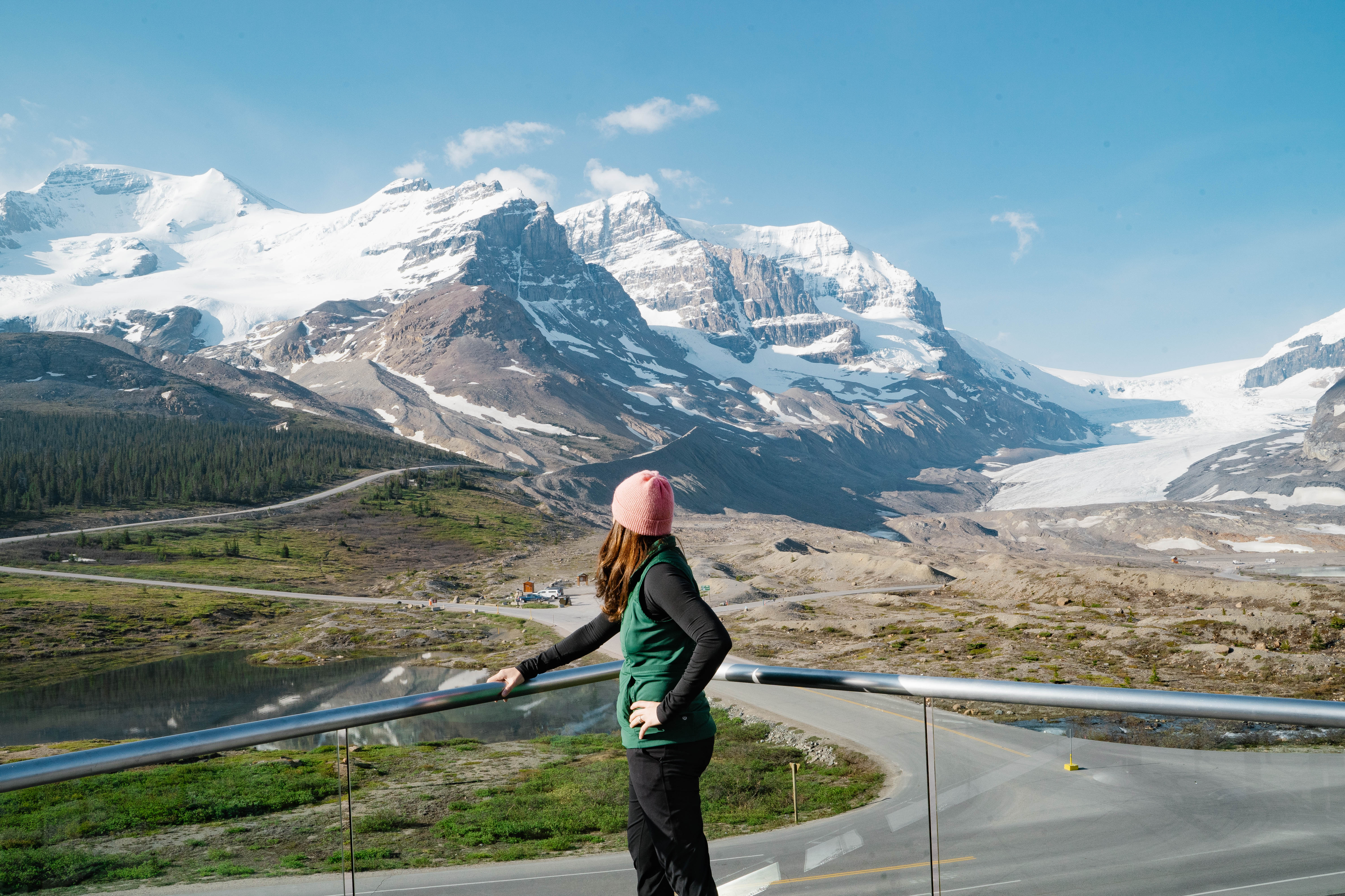 woman with her back turned to the camera, she is standing and looking at the sprawling glacier and mountain range
