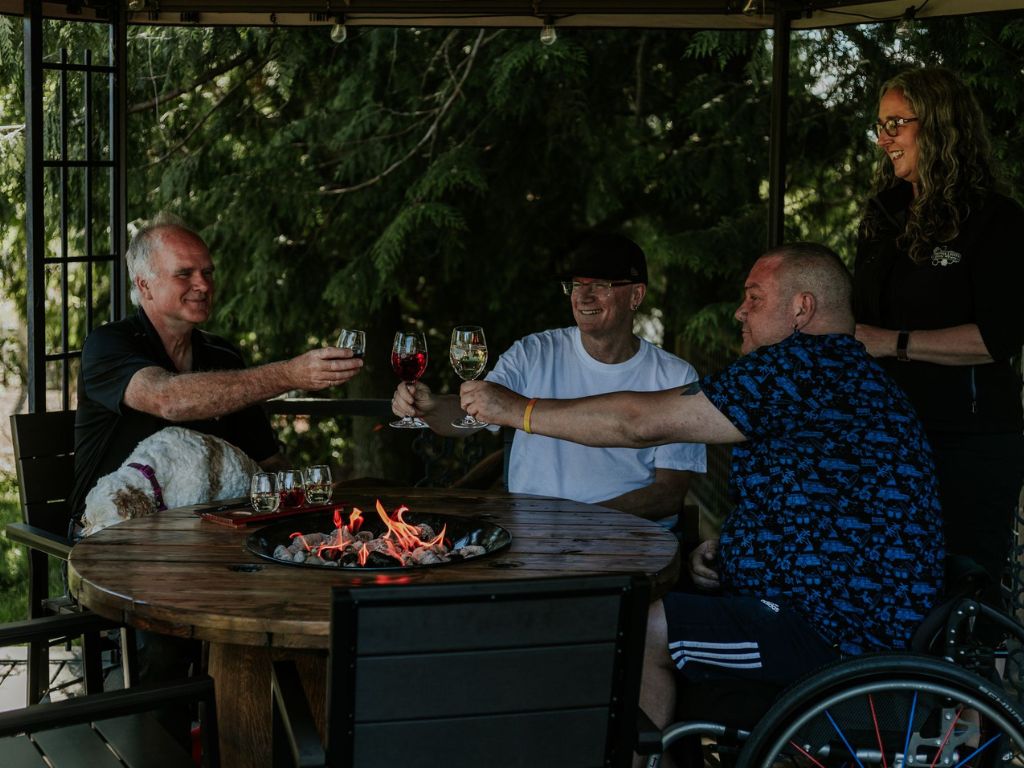 group of men holding up with wine glasses while sitting by a fire on the patio of Festina Lente Estate Winery