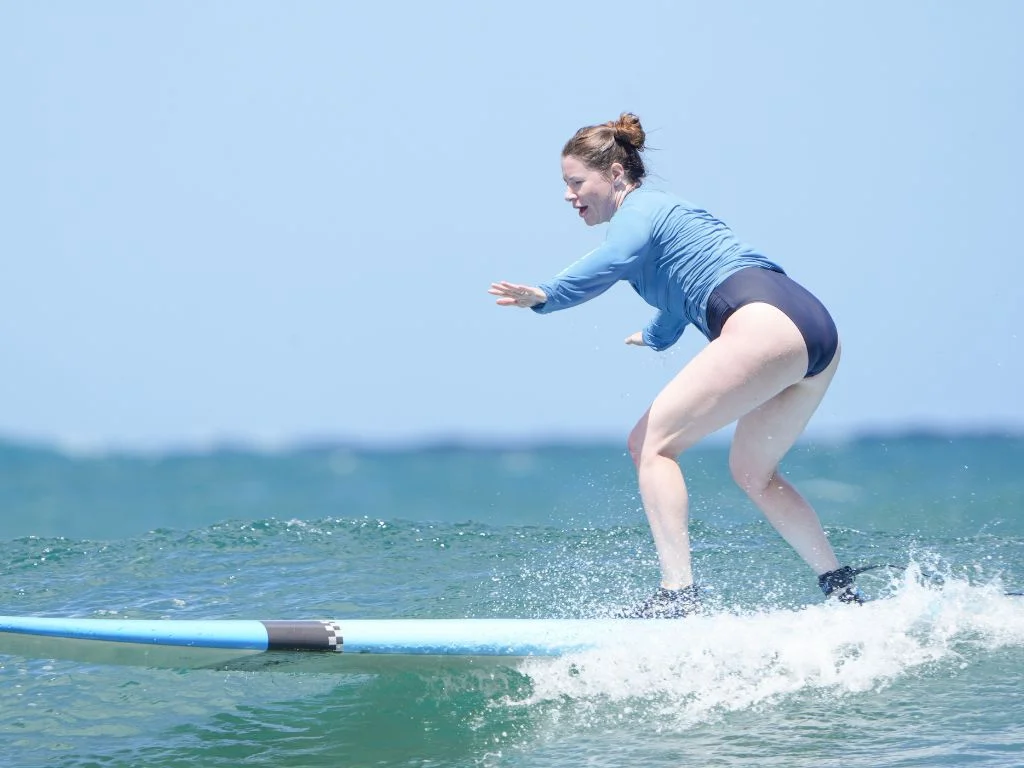 woman wearing a blue bathing suit and rash guard standing on a surf board during a lesson in hawaii